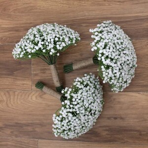 May include: Three white baby's breath bouquets tied with twine. The bouquets are arranged on a wooden surface.
