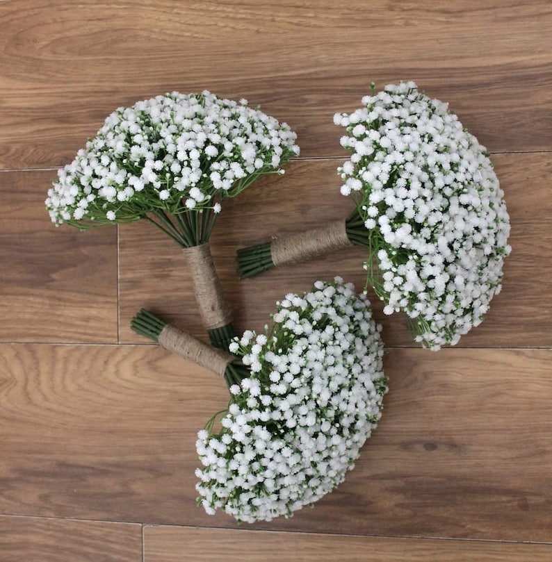 May include: Three white baby's breath bouquets tied with twine. The bouquets are arranged on a wooden surface.