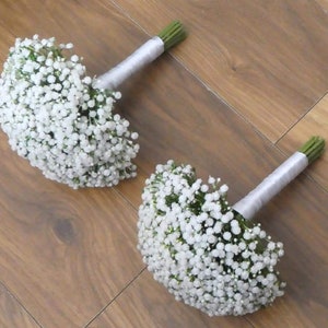 May include: Two white baby's breath bouquets tied with silver ribbon. The bouquets are arranged on a wooden surface.