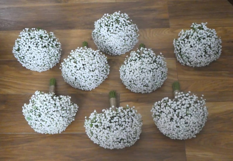 May include: Eight white baby's breath bouquets arranged on a wooden surface.