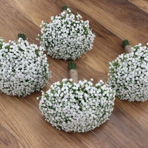 May include: Four white baby's breath bouquets tied with twine. The bouquets are arranged on a wooden surface.