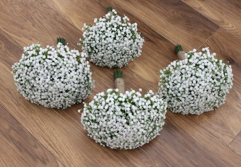 May include: Four white baby's breath bouquets tied with twine. The bouquets are arranged on a wooden surface.