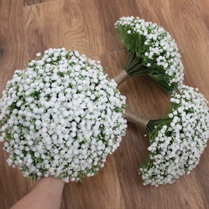 May include: Three white baby's breath bouquets tied with twine. The bouquets are arranged on a wooden surface.