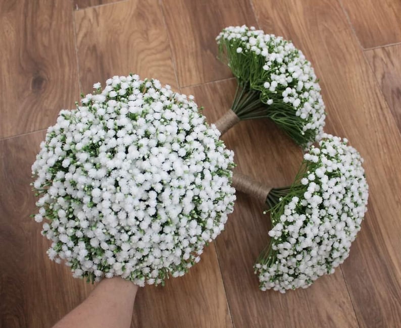 May include: Three white baby's breath bouquets tied with twine. The bouquets are arranged on a wooden surface.