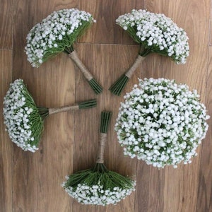 May include: Five white baby's breath bouquets tied with twine, arranged in a circle on a wood floor.