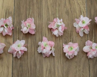 May include: Ten pink flower hair clips with gold bobby pins. The flowers are made of fabric and have a delicate, layered look.