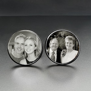 May include: Two round, silver-toned cufflinks, each featuring a black and white photograph. One cufflink displays a couple, the other shows an older couple. The cufflinks are set against a dark background.