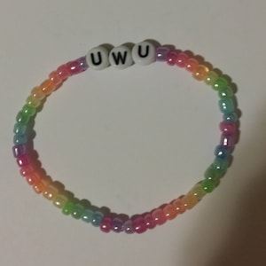 Può includere: Un braccialetto di perline arcobaleno con la parola "UWU" scritta con perline bianche. Il braccialetto passa attraverso sfumature di rosso, arancione, giallo, verde e viola.