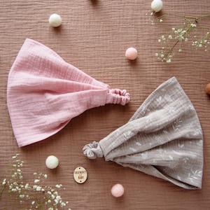 Op de afbeelding: Twee stoffen hoofdbanden, een roze en een beige met een wit bloemenpatroon. Beide hoofdbanden hebben een geknoopt elastiek aan de achterkant.