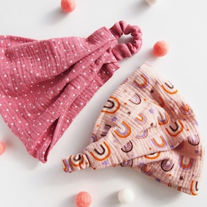 Op de afbeelding: Twee roze stoffen hoofdbanden met verschillende patronen. De ene hoofdband heeft witte stippen en de andere heeft een regenboogpatroon.