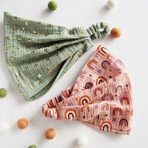 Op de afbeelding: Twee stoffen hoofdbanden, een groene met gouden sterren en een roze met regenboog- en sterpatronen.