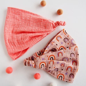 Op de afbeelding: Twee stoffen hoofdbanden, een roze met witte stippen en de andere roze met een regenboog- en sterrenpatroon.