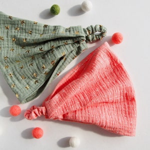 Op de afbeelding: Twee stoffen hoofdbanden, een groene met een gouden bladprint en een roze met witte stippen. Beide hoofdbanden hebben een geknoopte strik.