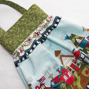 May include: A blue and white fabric tote bag with a green handle. The bag features a whimsical print of houses and trees.