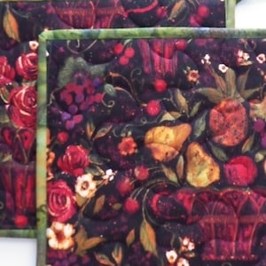 May include: Two square quilted pot holders with a dark background featuring a floral and fruit design. The design includes red roses, grapes, pears, and cherries. The edges are trimmed with a green and brown patterned fabric.