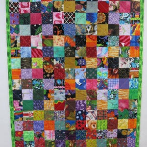 May include: A rectangular patchwork quilt featuring a grid of numerous small, multi-colored fabric squares with diverse patterns, including florals, geometric shapes, and animal prints, finished with a bright green fabric border.