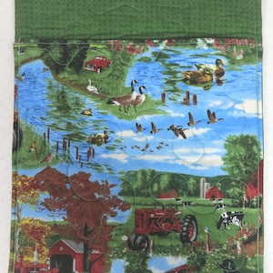 May include: A quilted fabric panel featuring a pastoral scene with a blue sky, water, and green fields. The design includes ducks, geese, a red tractor, a red car, and a red barn. The top edge is solid green.