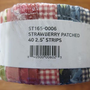 May include: A roll of fabric strips wrapped in clear plastic. The fabric features a patchwork design with red, white, and blue patterns. The label reads "STRAWBERRY PATCHED 40 2.5" STRIPS".