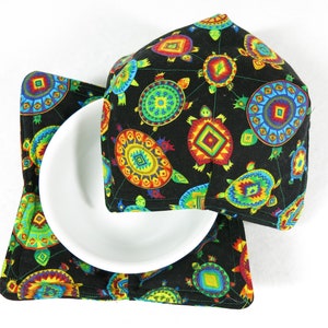 May include: Two black fabric pot holders with a colorful pattern of turtles and geometric designs. The pot holders are made of a quilted fabric and have a square shape.