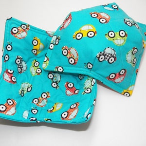 May include: Two turquoise blue fabric bowl cozies with a pattern of colorful cars. The cozies are quilted and have a square shape.