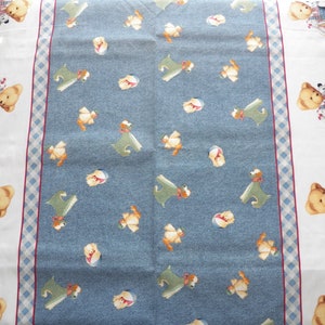 Pode incluir: Um tecido estampado azul claro e branco com uma borda de ursinhos de pel&uacute;cia e um desenho central de c&atilde;es de desenho animado e outros personagens. O tecido tem uma borda xadrez e uma faixa vermelha.
