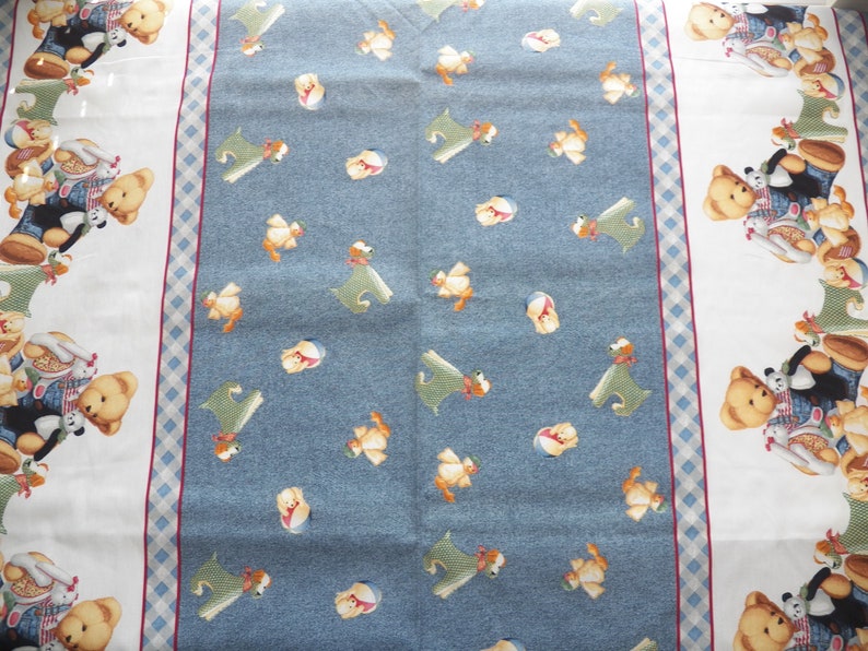 Pode incluir: Um tecido estampado azul claro e branco com uma borda de ursinhos de pel&uacute;cia e um desenho central de c&atilde;es de desenho animado e outros personagens. O tecido tem uma borda xadrez e uma faixa vermelha.