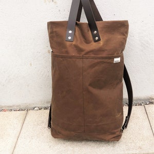 Pu&ograve; includere: Una borsa tote in tela marrone con manici in pelle e una tracolla in pelle marrone. La borsa ha una grande tasca sul davanti e una piccola etichetta con la parola "Kikki" su di essa.