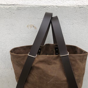 Pu&ograve; includere: Una borsa tote in tela marrone con due lunghi cinturini in pelle marrone. I cinturini hanno fibbie in metallo argentato.