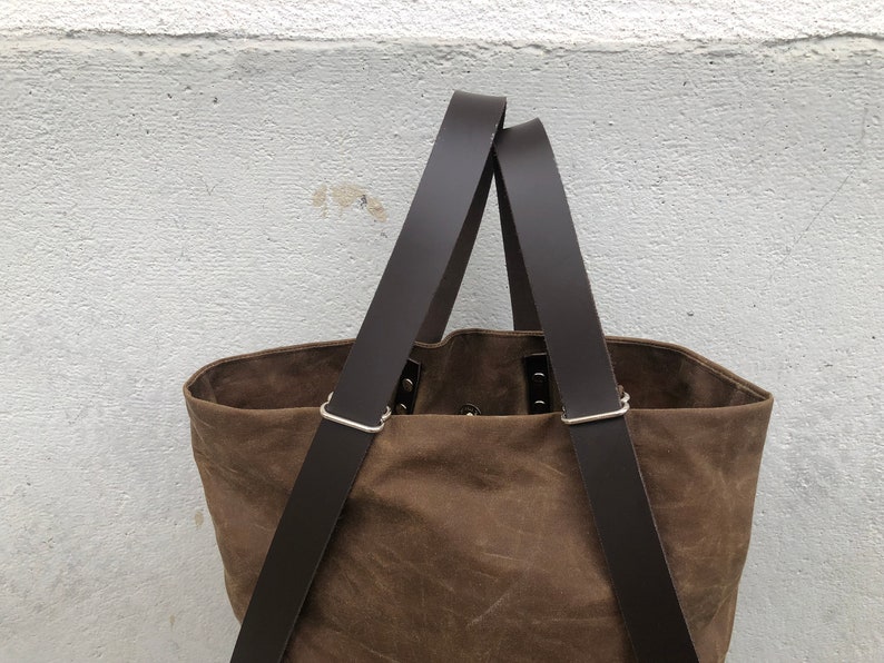 Pu&ograve; includere: Una borsa tote in tela marrone con due lunghi cinturini in pelle marrone. I cinturini hanno fibbie in metallo argentato.