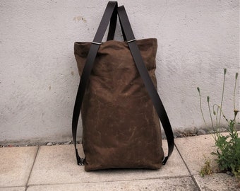 May include: A brown canvas tote bag with black leather straps. The bag is sitting on a concrete surface.