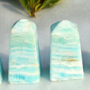 May include: Four polished, rectangular gemstone towers. The stones have a layered appearance with bands of light blue, white, and hints of yellow. The tops are rounded and angled. The stones are displayed on a light surface.
