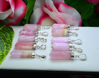 May include: A collection of pink quartz crystal pendants with silver-colored metal caps and loops. The crystals vary in shades of pink and are displayed on a white surface, with pink and white flowers in the background.