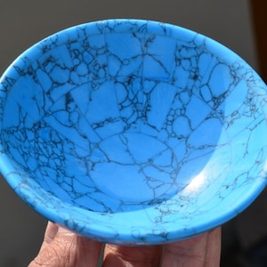 May include: A round, shallow bowl with a vibrant turquoise color and a striking black veining pattern. The bowl's surface has a smooth, polished finish, enhancing the visual appeal of the unique stone-like design. This decorative bowl is ideal for holding small items.