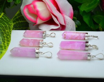 May include: Seven pink crystal pendants with silver-colored metal caps and loops. The crystals are a light pink color and are faceted. The pendants are arranged on a white surface, with a pink and white flower and green leaves in the background.