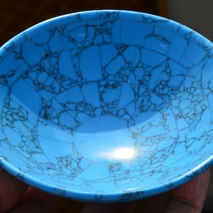 May include: A vibrant turquoise bowl with a unique, cracked pattern in dark gray. The bowl's smooth, glossy surface reflects light, highlighting its rounded shape. This decorative bowl is ideal for holding small items or as a display piece.