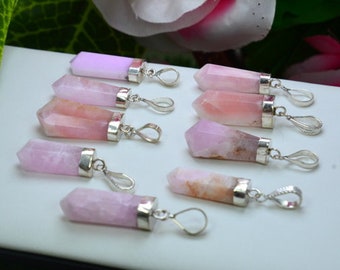May include: A collection of pink and rose quartz crystal pendants with silver-colored metal caps and loops. The crystals vary in color, from light pink to a deeper rose hue. The pendants are arranged on a white surface.