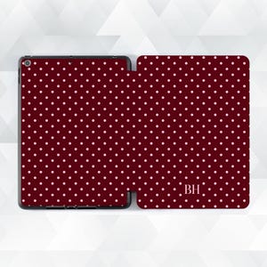 May include: A burgundy tablet case with a repeating pattern of small, light pink polka dots. The case is open, revealing the tablet screen and the interior. The initials "BH" are visible on the cover.
