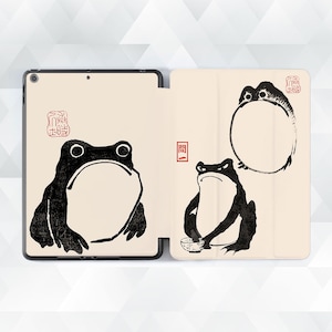 May include: A black and white illustration of three frogs on a cream-colored background. The frogs are in different poses, one is sitting, one is standing, and one is in a circle. The background has a Japanese character on it.