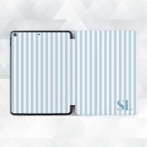 May include: An open tablet case with a light blue and white striped pattern. The case is open, revealing the tablet screen. The cover has the initials "SL" in the bottom right corner.
