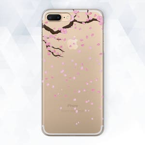 May include: A clear phone case with a gold background and a design of a pink cherry blossom branch with falling petals. The text "iPhone" is printed on the case.