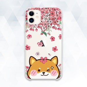 May include: Clear phone case with a pink and white floral design and a cartoon Shiba Inu dog with brown fur and pink cheeks. The dog is looking to the right.