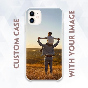 May include: A clear phone case with a photo of a father carrying his child on his shoulders. The photo shows the two walking through a field of tall grass.