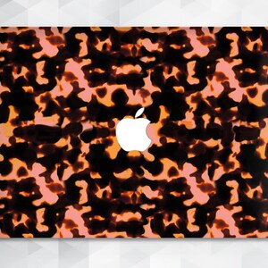 Może przedstawiać: Skórka na laptopa z wzorem w stylu pancerza żółwia w odcieniach brązu, pomarańczy i różu. Skórka ma białe logo Apple w środku.