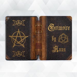 Peut inclure: Une coque de tablette marron foncé avec un design de livre vintage. La couverture présente des symboles dorés en relief, dont un pentagramme, des croissants de lune et le texte "Grimoire by Anna". La tranche est de couleur marron clair.