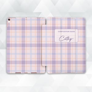May include: A tablet case with a pastel plaid pattern in shades of purple, peach, and blue. The case is open, revealing the tablet inside. The cover features a label that reads "Composition Book" and the name "Cathy".