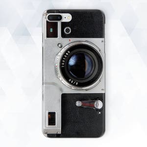 Puede incluir: Una funda para teléfono con diseño de cámara vintage, con acabado de cuero negro y lente de cámara plateada. La lente tiene un anillo plateado con números alrededor. La funda tiene un diseño negro y plateado.