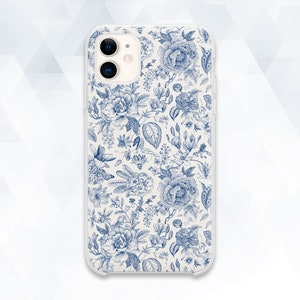 Puede incluir: Una funda de teléfono blanca con un patrón floral azul. La funda tiene una parte posterior transparente y un borde blanco. La funda del teléfono tiene un recorte para la cámara en la parte posterior.