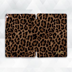 May include: A brown and black leopard print tablet case. The case is open, revealing the interior and exterior design. The name "Millie" is written in gold script on the lower right side of the case.