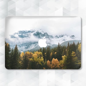 May include: A laptop skin with a scenic mountain landscape featuring a snowy peak, a forest of evergreen trees, and a white apple logo.