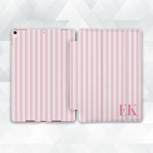 Może przedstawiać: Różowo-białe etui na iPada w paski, otwarte, aby pokazać urządzenie i zamknięte, aby pokazać okładkę. Okładka ma inicjały "EK" w prawym dolnym rogu. Etui ma chronić iPada.